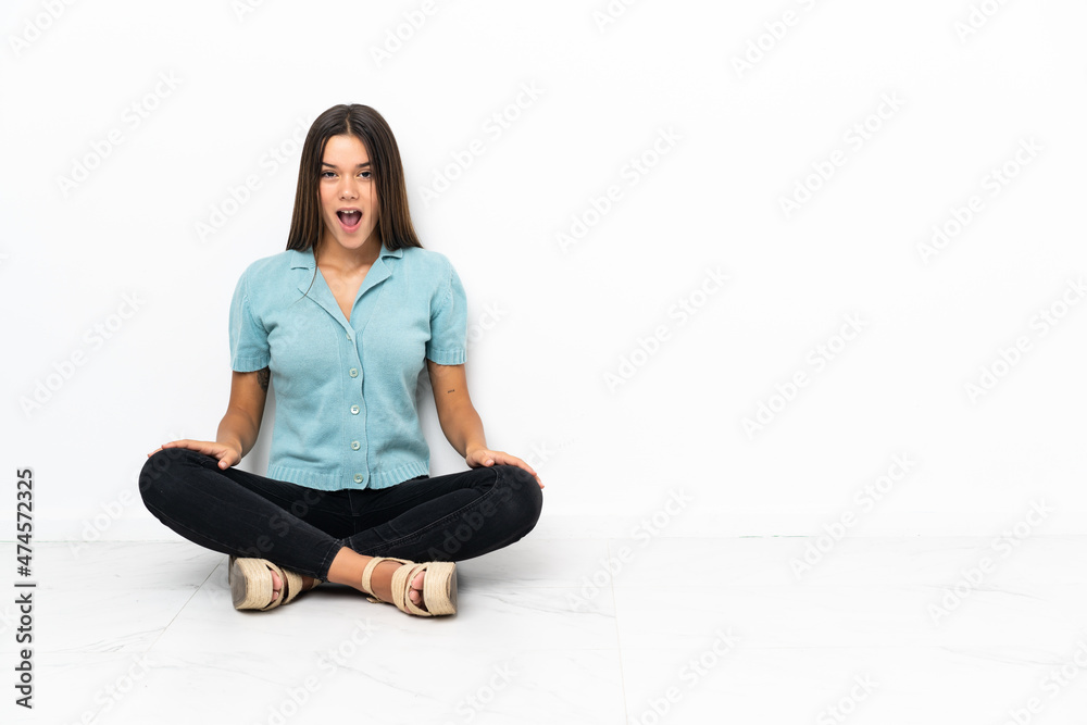 Teenager girl sitting on the floor with surprise facial expression Teenager girl sitting on the floor with surprise facial expression