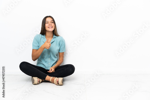 Teenager girl sitting on the floor giving a thumbs up gesture