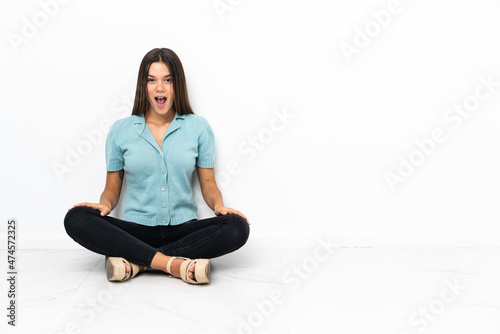 Teenager girl sitting on the floor with surprise facial expression