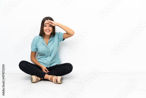 Teenager girl sitting on the floor looking far away with hand to look something