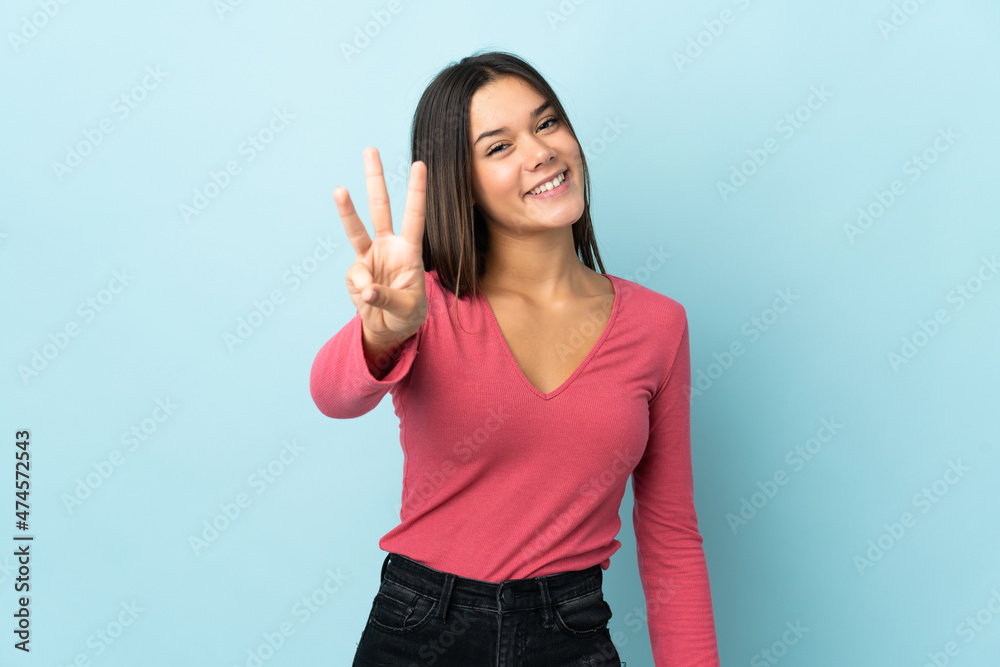 Teenager girl isolated on blue background happy and counting three with fingers Teenager girl isolated on blue background happy and counting three with fingers