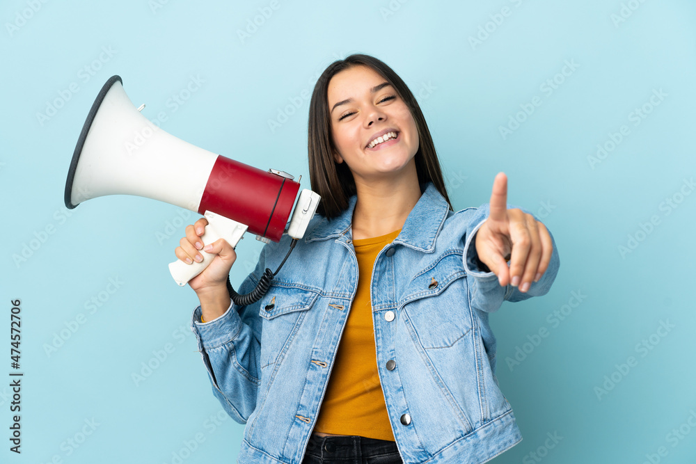 Teenager girl isolated on yellow background holding a megaphone and smiling while pointing to the front Teenager girl isolated on yellow background holding a megaphone and smiling while pointing to the front
