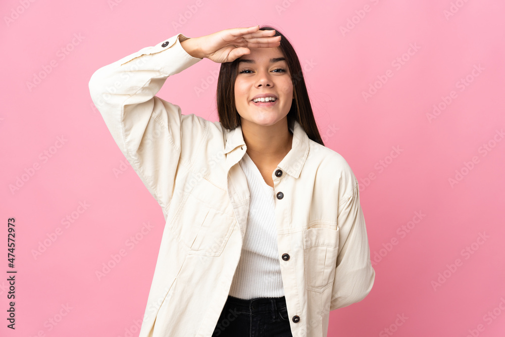 Teenager girl isolated on pink background looking far away with hand to look something