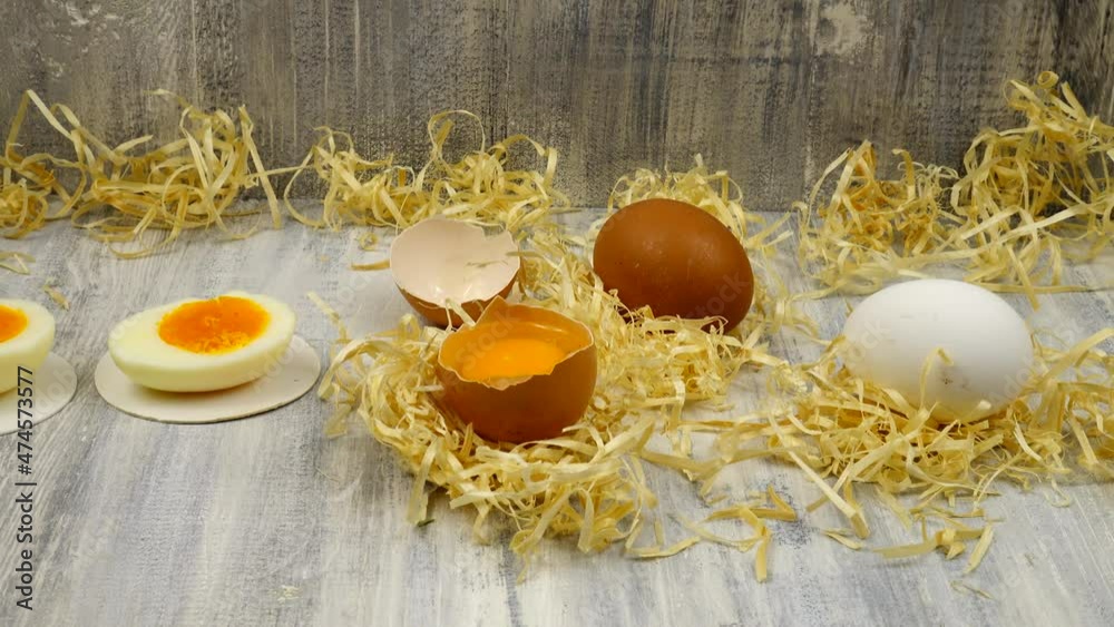 Chicken eggs, white and brown, raw and boiled, whole and cut in two, in eggshell and peeled, lie on a wooden table.