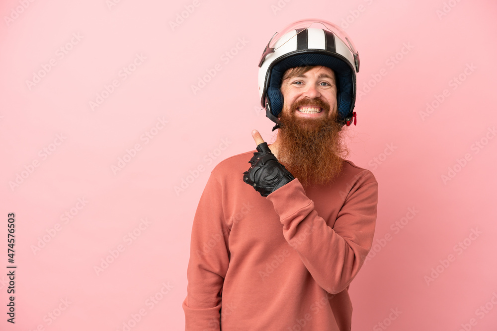 Young reddish caucasian man with a motorcycle helmet isolated on pink background pointing to the side to present a product