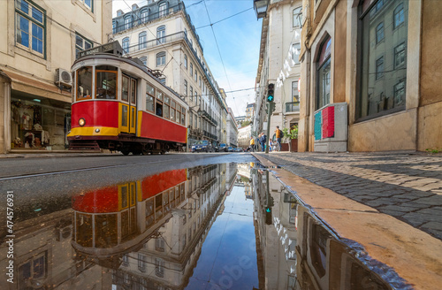 Red tram in Lisbon, Portugal, with reflection in puddle. Implying travel and holidays / vacations in Europe.