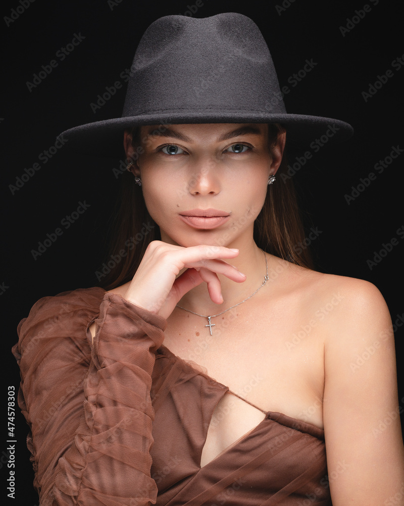Fashionable studio portrait of a beautiful young girl in black hat on a black background. Low key. Fashionable studio portrait of a beautiful young girl in black hat on a black background. Low key.