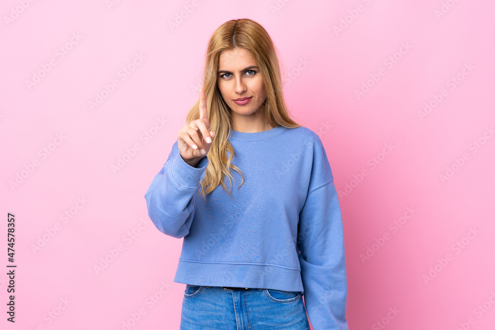 Young Uruguayan blonde woman over isolated pink background counting one with serious expression Young Uruguayan blonde woman over isolated pink background counting one with serious expression
