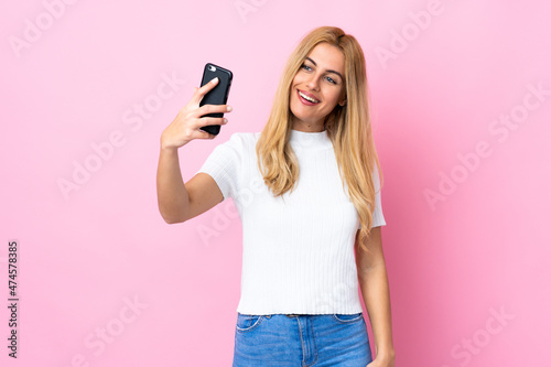 Young Uruguayan blonde woman over isolated pink background making a selfie