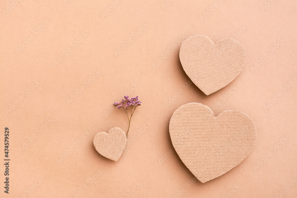 Fototapeta premium Family concept. Three cardboard hearts - dad, mom and baby with a dry flower on a beige background. Top and vertical view.