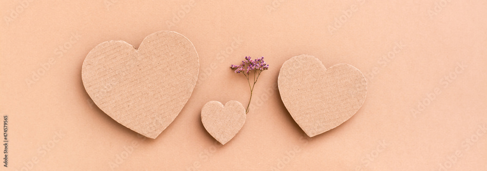 Obraz premium Family concept. Three cardboard hearts - a child with a dry flower between parents on a beige background. Top view. Web banner