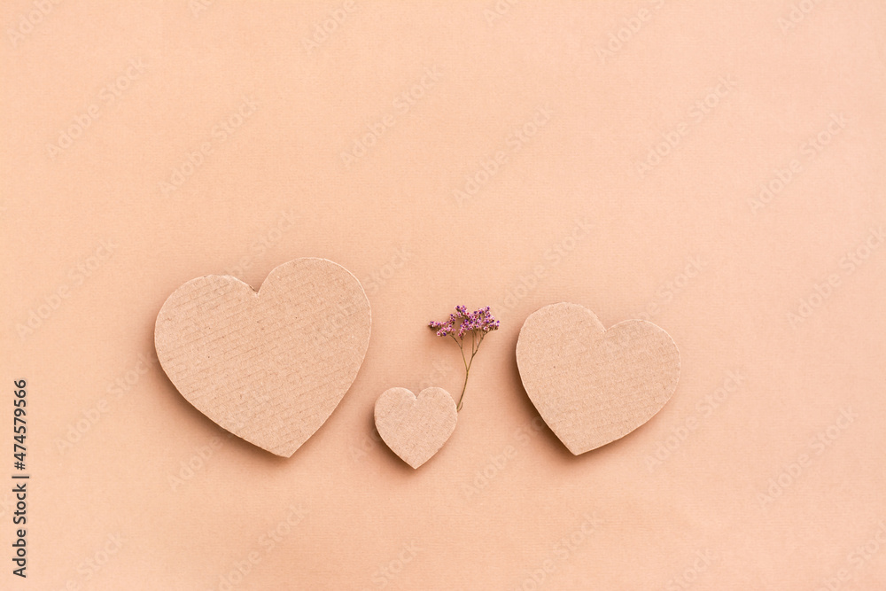 Obraz premium Family concept. Three cardboard hearts - a child with a dry flower between parents on a beige background. Top view.