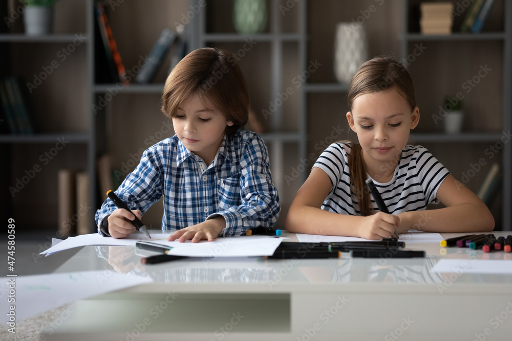 Happy adorable two children boy girl drawing in paper albums, sitting at table in living room, involved in coloring pictures with markers, enjoying creative activity, developing art skills at home. Happy adorable two children boy girl drawing in paper albums, sitting at table in living room, involved in coloring pictures with markers, enjoying creative activity, developing art skills at home.