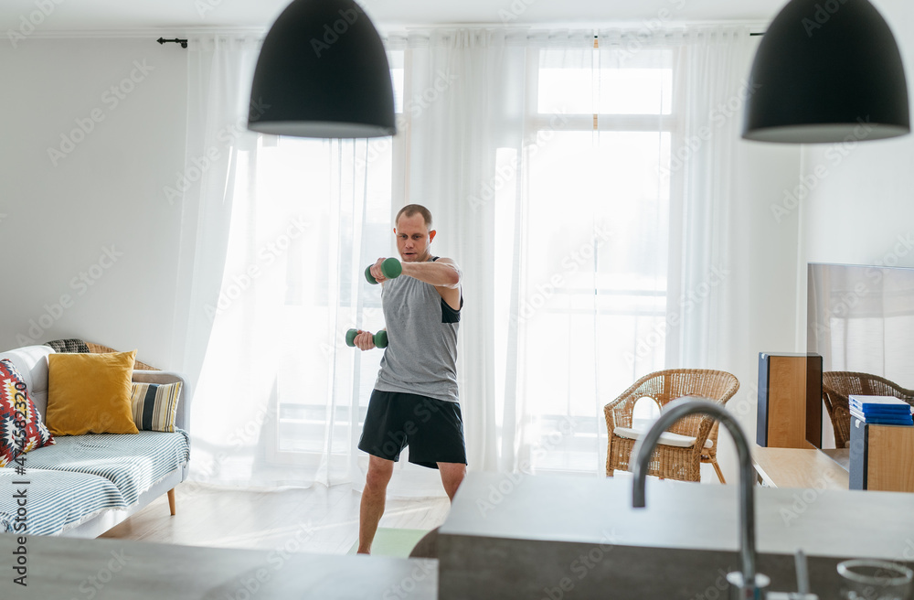 Home workout in the living room. Young muscular body man doing arm exercises using dumbbells. Healthy lifestyle or sporty people concept image. Home workout in the living room. Young muscular body man doing arm exercises using dumbbells. Healthy lifestyle or sporty people concept image.