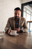 Businessman using smartphone while drinking coffee in a cafe