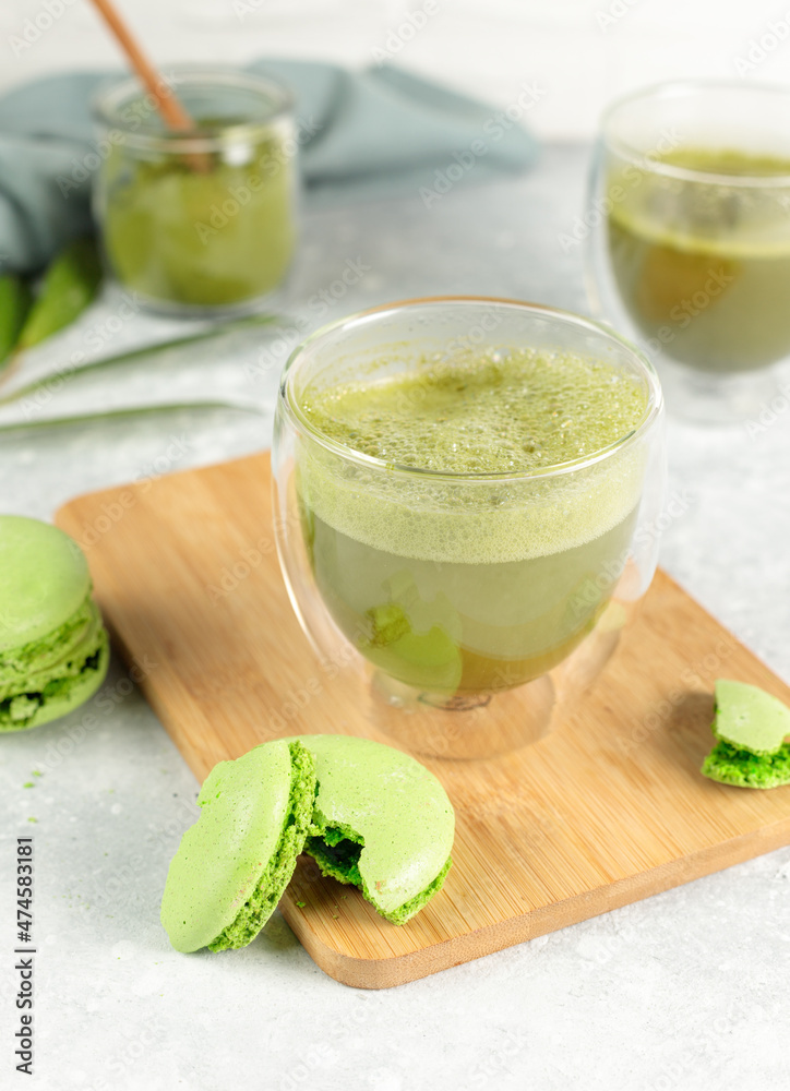 Matcha tea in a glass and green macaroon cake on a wooden bamboo tray. Close-up on a gray background. Matcha tea in a glass and green macaroon cake on a wooden bamboo tray. Close-up on a gray background.