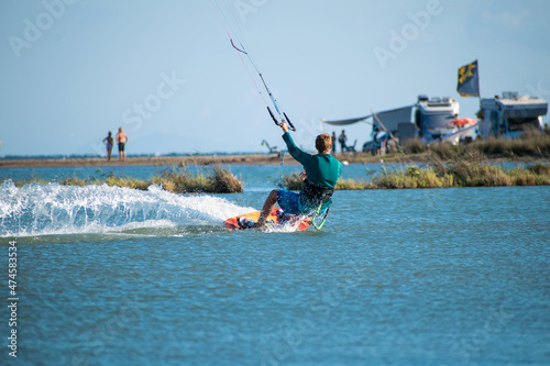 Kitesurfer athlete surfing on sea surface close to campervans