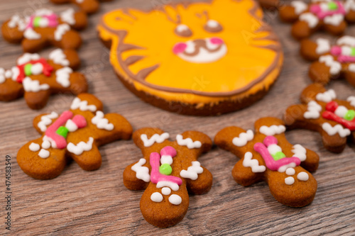 Close-up of a gingerbread men with glaze put around the tiger-shaped orange gingerbread cookie on a wooden table.