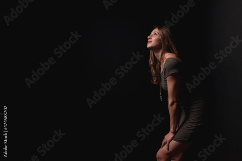beautiful young model posing leaning against the wall in a black studio background with the light coming from above, with a casual but elegant style