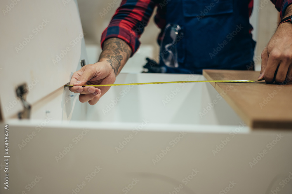 Young male carpenter working in workshop and measuring with meter Young male carpenter working in workshop and measuring with meter