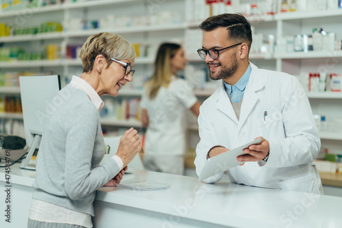 Young male pharmacist giving prescription medications to senior female customer in a pharmacy photo
