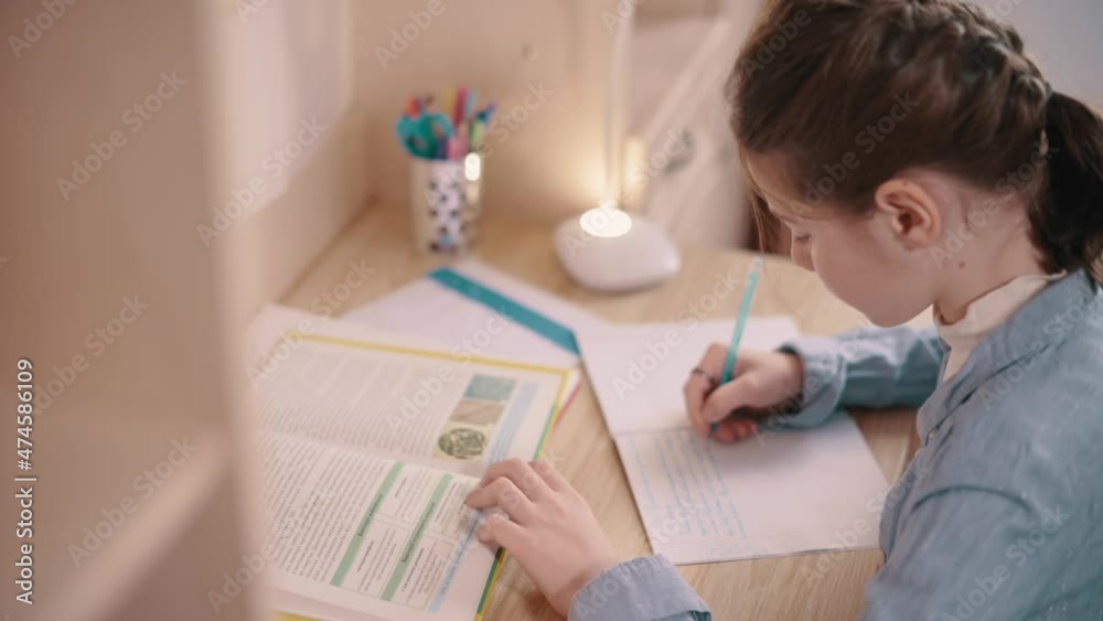 Girl doing homework. Girl writes in notebook at table in her room. Girl doing homework. Girl writes in notebook at table in her room.