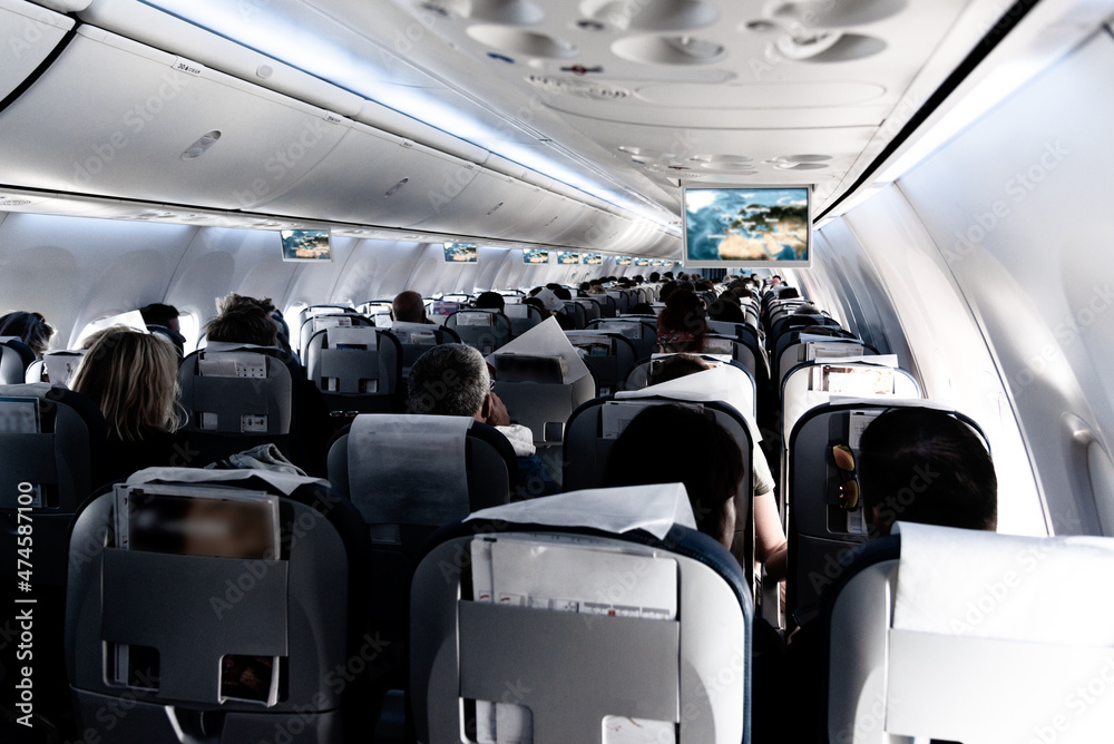 Fototapeta premium Passenger cabin of commercial aircraft with unrecohnizable travellers seated on their seats during flight.