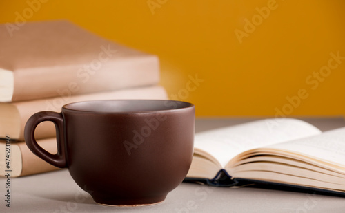 desk with cup of coffee or tea with hot steam , open books, orange yellow background