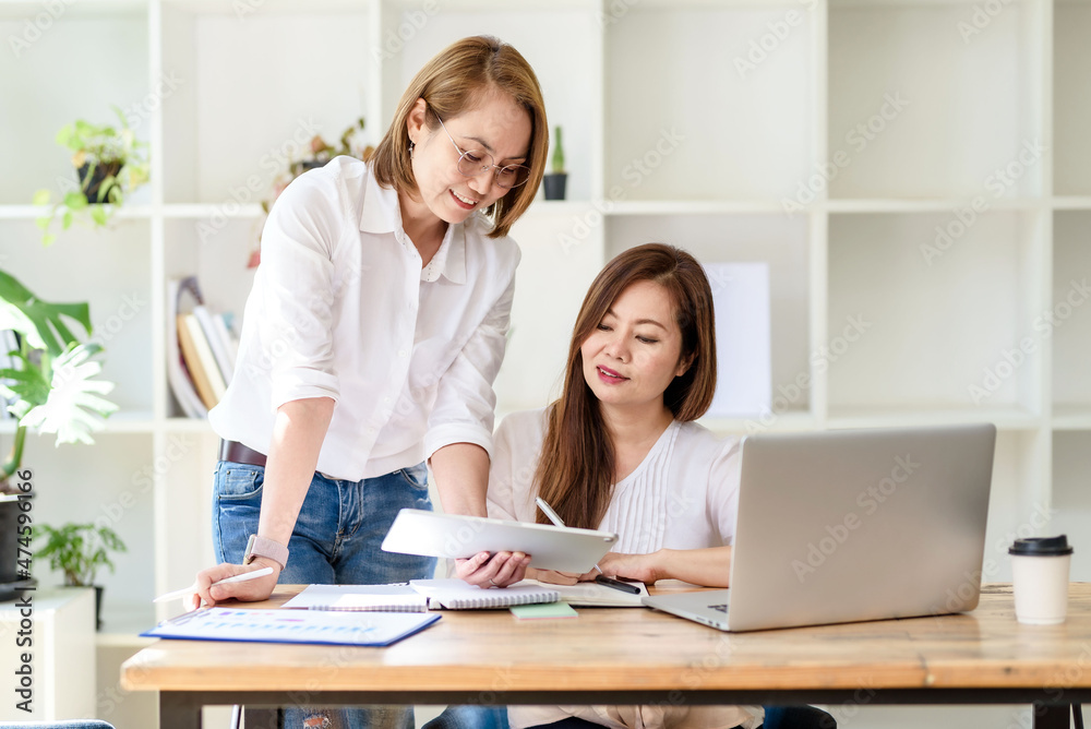 Two smiling middle-aged Asian businesswoman discussing and working laptop computer in the office. Two smiling middle-aged Asian businesswoman discussing and working laptop computer in the office.