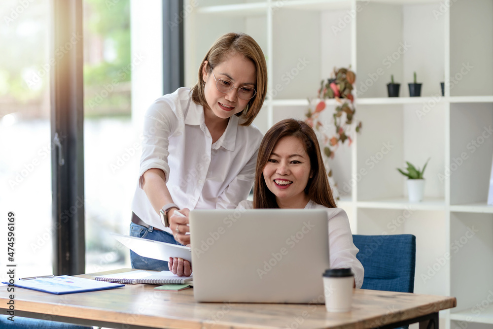 Two smiling middle-aged Asian businesswoman discussing and working laptop computer in the office. Two smiling middle-aged Asian businesswoman discussing and working laptop computer in the office.
