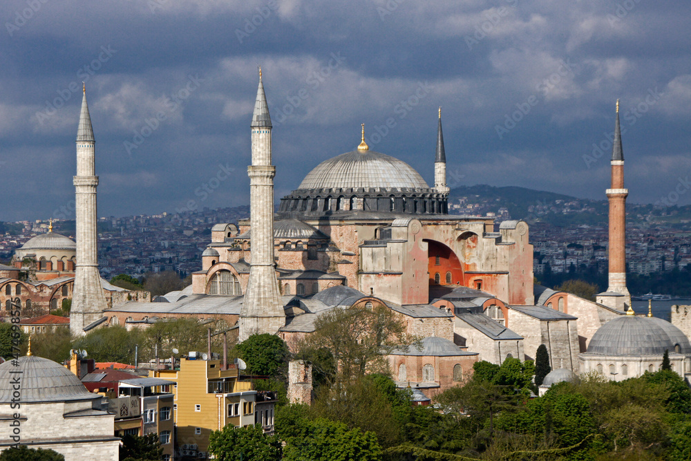 Fototapeta premium Istanbul, Turkey: Minarets of a local mosque and the orange-walled Hagia Sophia Museum rise into a cloudy sky above Hagia Eirene at Topkapi Palace Museum.
