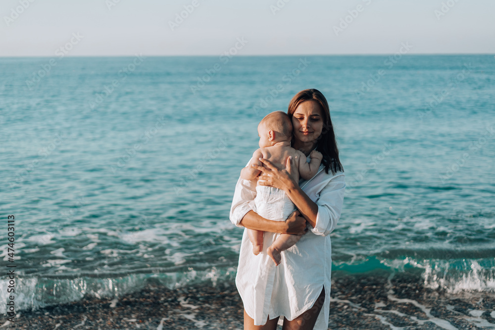 A young mother walks along the beach with a small child in diapers. Mother day. Family with one child. Happy childhood with mommy. Walking ocean wave