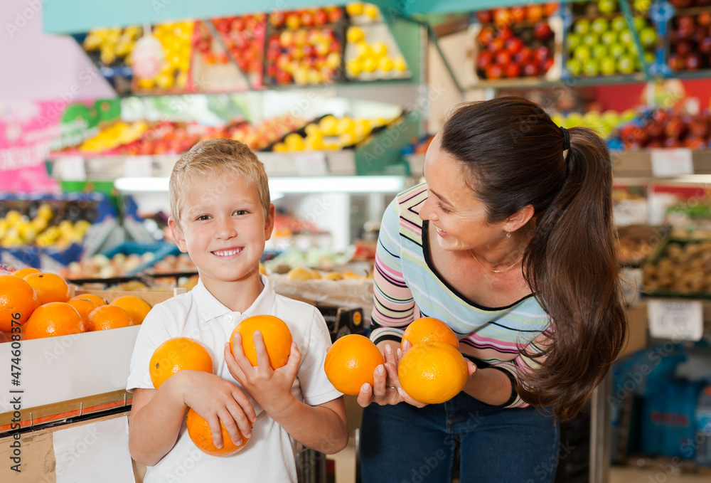 Fototapeta premium .Little child with his mother choosing fresh oranges at fruit department of supermarket