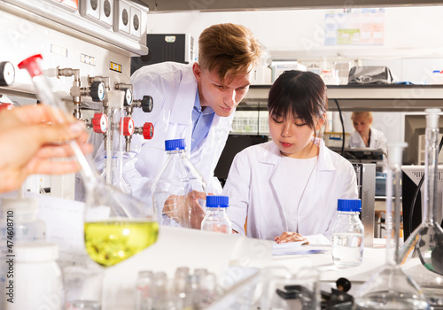 Chinese female student with male groupmate performing experiments in university chemistry laboratory, recording results in workbook