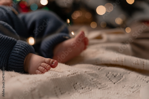 bare feet of a baby in a blue knitted jumpsuit lying on a light blanket on the floor under the Christmas tree closeup. winter holiday  funny moments  child christmas. High quality photo