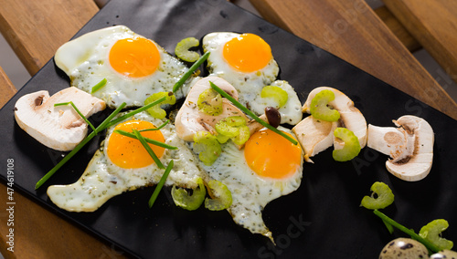 Delicious broken quail eggs with green onion and sliced champignons on black serving board photo