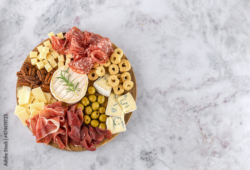 Top view of tasty charcuterie board with cheese, grape, nuts, olives, and ham on a circle kitchen plate on the marble stone background, top view, copy space. Gourmet food, copy space. photo