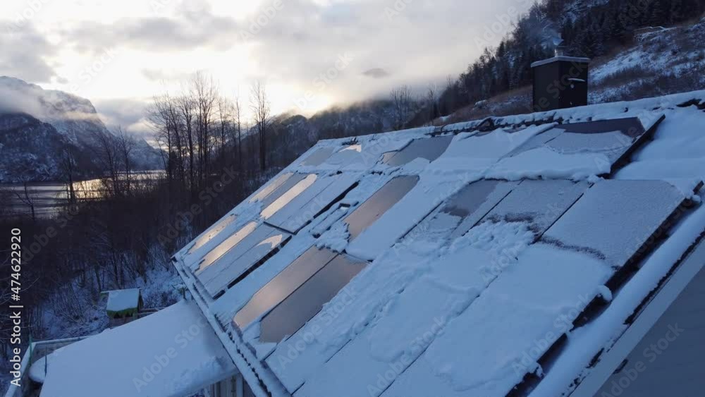 Solar panels on private home covered in snow - Smoke from chimney with stunning fjord landscape background - Beautiful sunrise reflections in solar panels - Norway Solar panels on private home covered in snow - Smoke from chimney with stunning fjord landscape background - Beautiful sunrise reflections in solar panels - Norway