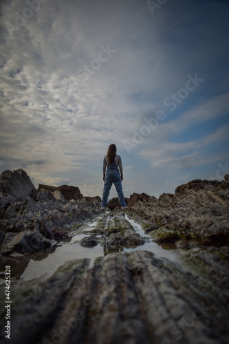 girl in denim overalls  looking towards the sea on some stones