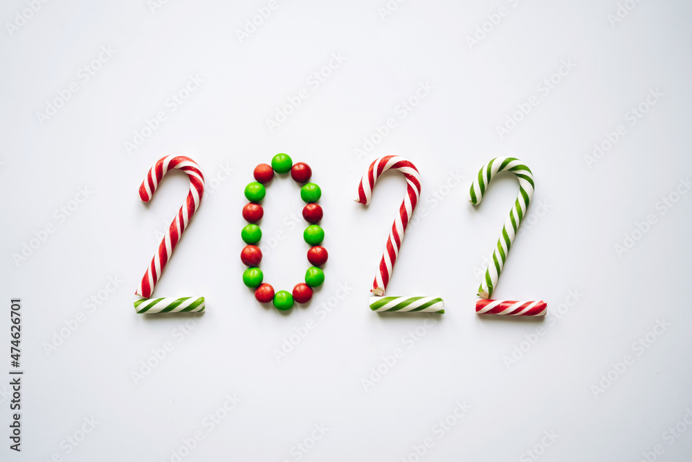 Fototapeta premium Year 2022 laid out from round multicolored candies and striped candy canes on white background