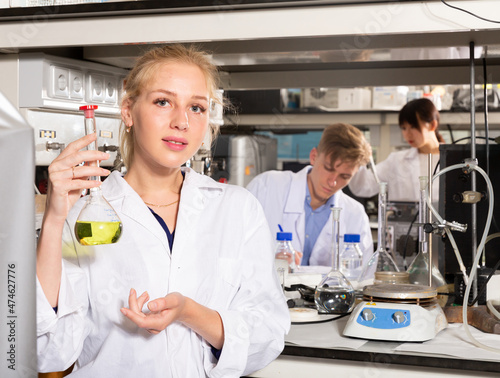 Attractive female student performing experiments in university laboratory, examining chemical substances in glass lab flask