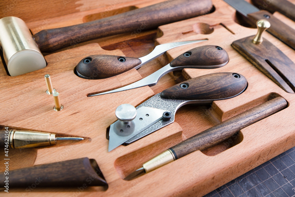 Exclusive handmade leather craft tools. Close up of different tanner tools on wooden box. Set of Different knifes from steel and wood. Black background. Exclusive handmade leather craft tools. Close up of different tanner tools on wooden box. Set of Different knifes from steel and wood. Black background.
