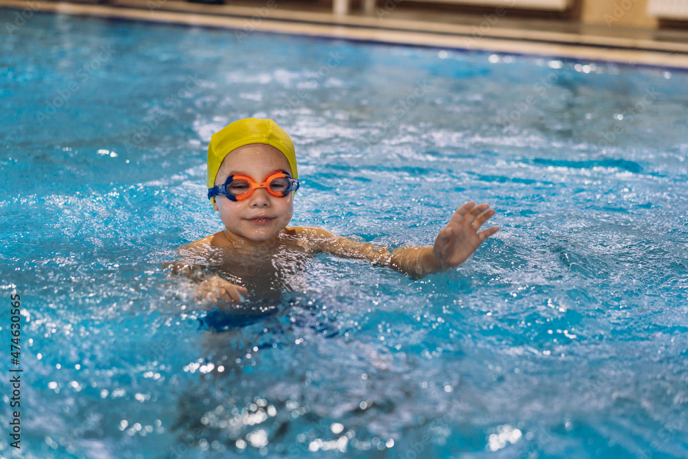 little caucasian boy wearing goggles looking learning to swim in a pool