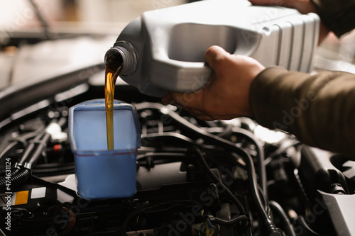 A man pours engine oil from a canister into a car