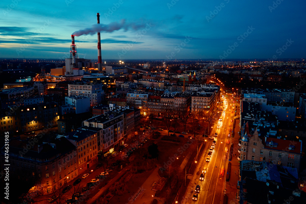 Fototapeta premium Aerial view of night city with smoking pipes, steam frome pipe to heating residential buildings at winter season