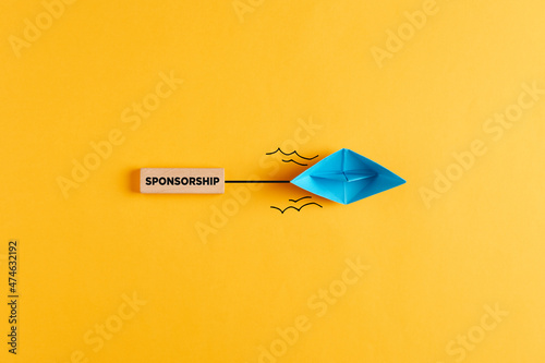 Paper boat pulls a wooden banner with the word sponsorship. Sponsoring, financial support or fundraising photo