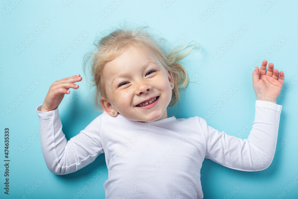 Beautiful smiling blonde girl lying on a blue background. Top view, flat lay Beautiful smiling blonde girl lying on a blue background. Top view, flat lay
