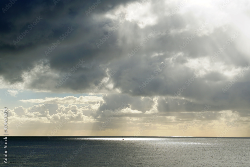 Morning over the ocean. The clouds and the sun breaks through the thick veil. A distant yacht in the rays of sunlight. Glare on the water
