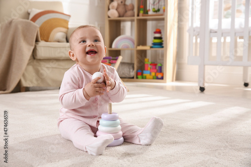 Cute baby girl playing with toy pyramid on floor at home