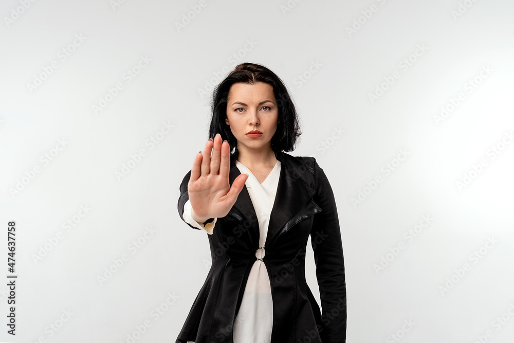 Serious young businesswoman in black formal jacket white shirt showing stop gesture with palm isolated on white background. Business concept Serious young businesswoman in black formal jacket white shirt showing stop gesture with palm isolated on white background. Business concept